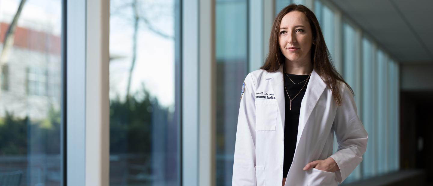 Student standing in O'Dowd Hall in her OUWB white coat